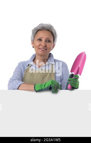 Mature asian woman gardener with scoop standing behind blank banner with empty copy space for text isolated on white background Stock Photo