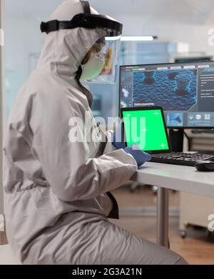 Chemist man wearing protection suit holding tablet with green mockup. Team of microbiologists doing vaccine research writing on device with chroma key, isolated display. Stock Photo