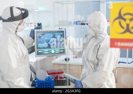 Team of scientist looking at virus evolution standing in lab danger zone dressed in ppe suit. Group of doctors examining vaccine evolution using high tech for diagnosis against covid19. Stock Photo