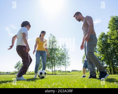 Parents and kids playing football soccer outdoors on summer meadow Stock Photo