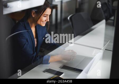Gorgeous business lady wearing dark blue jacket looking to the screen of laptop in room indoors Stock Photo