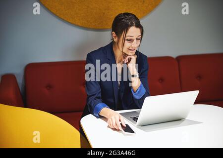 Beautiful young female graphic designer working at the netbook while surfing internet in room indoors Stock Photo