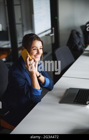 Brunette Caucasian female social media manager talking on cell phone in start-up office Stock Photo