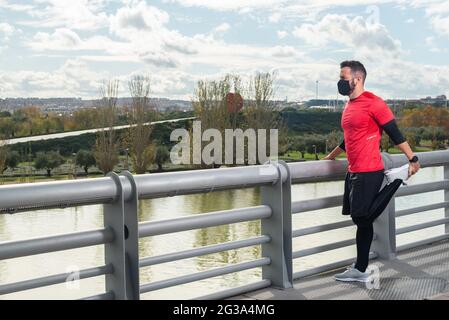 Young runner man with mask stretching in a park Stock Photo