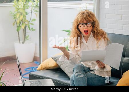 woman at home with computer surprised looking at papers Stock Photo