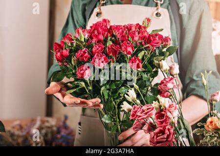 Woman florist is holding a large bouquet of roses. Florist workplace. Small business concept. Flowers and accessories shop. Close-up Stock Photo