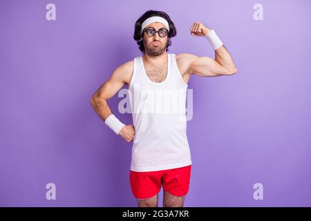 Photo of crazy funny sportsman puffed cheeks demonstrate muscle wear glasses sportswear isolated purple background Stock Photo