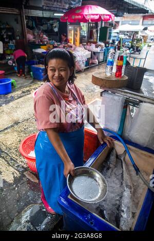 A woman in a Bangkok street market adds ice to a chest of keep fresh fish chilled. Stock Photo