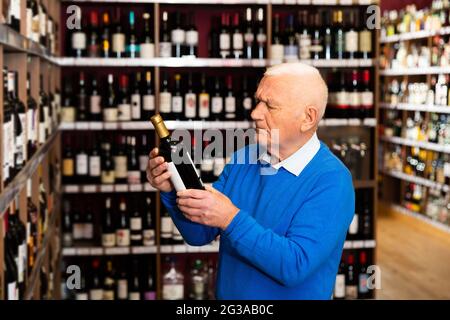 Elderly man chooses red wine in a liquor store Stock Photo