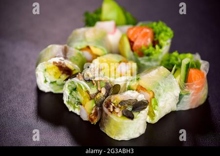 rice paper rolls with salmon, lettuce, shrimp, cucumber, avocado and cream cheese philadelphia on black background. Spring rolls Stock Photo