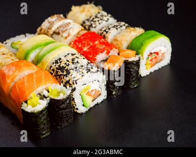 Sushi set, close up view. Various sushi roll with salmon, avocado, cream cheese philadelphia and tobiko flying fish caviar on black background with re Stock Photo