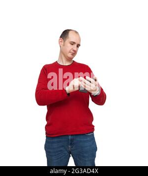 A bald young man is typing a message with his mobile phone. The person is dressed in a red sweater, jeans and wears a watch. The background is white. Stock Photo