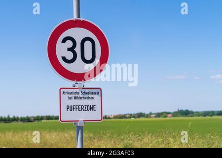 A traffic sign for speed limit and the additional sign in German language , African swine fever in wild animals , buffer zone Stock Photo
