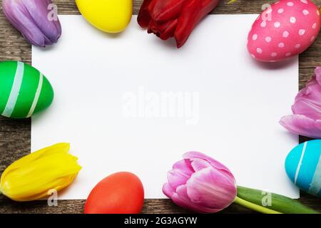 Hand-painted easter eggs with tulips on blank greeting card over wooden background copy space for text Stock Photo