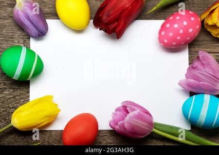 Hand-painted easter eggs with tulips on blank greeting card over wooden background copy space for text Stock Photo