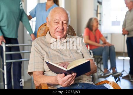 Satisfied senior man sitting in armchair relaxing reading a book in retirement home Stock Photo