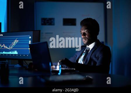Black employee working on laptop in dark office Stock Photo