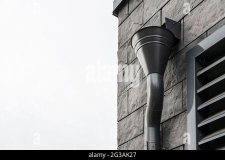 roof gutter mounted on the wall of the building lined with modern stone tiles, black and brown stylish color, modern design element close-up. Stock Photo