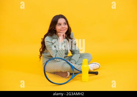 smiling child sit in sportswear with squash racquet and water bottle on yellow background, sport Stock Photo