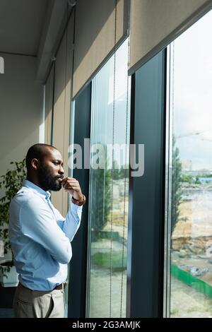 thoughtful african american businessman looking away while standing near window Stock Photo