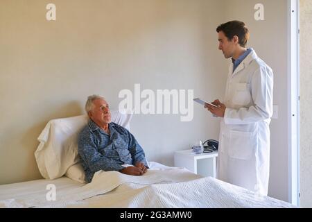 Carer or young doctor on bedside rounds of a senior in hospital Stock Photo
