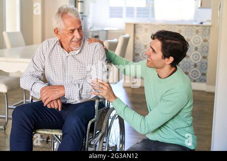 Smiling man taking care of senior man in wheelchair in assisted living project Stock Photo