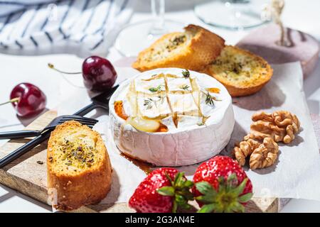 Baked cheese Camembert or Brie with thyme and maple syrup. Cheese, fruits, bread and nuts to white wine. Stock Photo