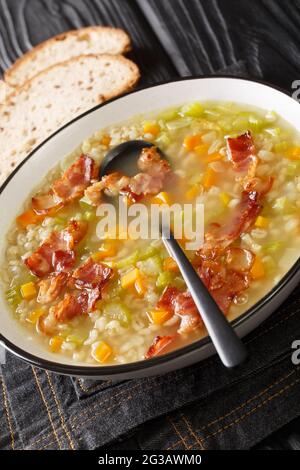 Gerstensuppe is a soup made of barley with a few vegetables and a bit of speck close up in the plate on the table. Vertical Stock Photo
