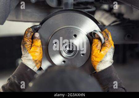 Closeup male tehnician mechanic greasy hands in gloves install new car oem brake steel rotor disk during service at automotive workshop auto center Stock Photo