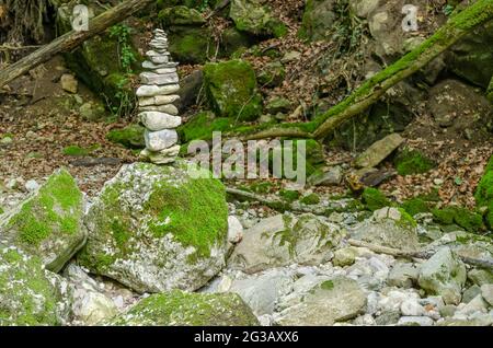 Single rock stack in a streambed. Pile of stacked rocks balancing on a big rock in a bed of a wild stream. Rocks laid flat upon each other. Stock Photo