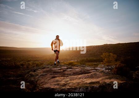 Young fit male athlete running over rocky mountain trail on hill during sunrise Stock Photo
