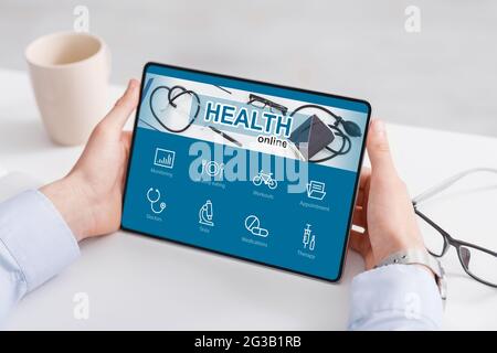 Unrecognizable businessman checking health app on digital tablet while working in office, sitting at worktable, monitoring his health condition during Stock Photo