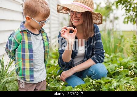 Child and mother gardening in strawberry plant garden in backyard