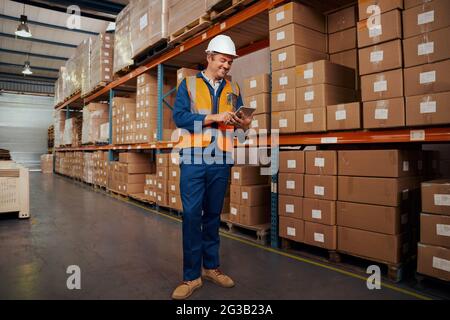Cheerful male warehouse supervisor standing in warehouse using smart tablet Stock Photo