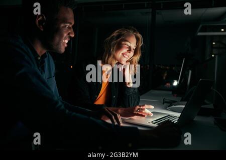 Diverse creative business people working with laptop overtime at night in low light at office Stock Photo