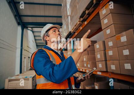 Warehouse manager in uniform and hardhat checking the stock using digital tablet Stock Photo
