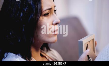 portrait of upset woman holding photo frame and crying on sofa at home Stock Photo