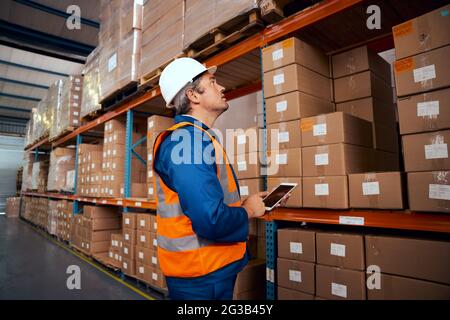 Male technician in safety work wear keeping stock records in digital tablet Stock Photo