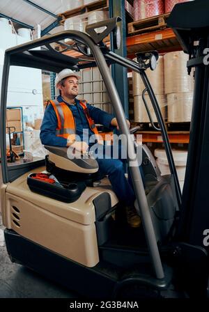 Portrait of a happy warehouse worker sitting in forklift truck at large warehouse Stock Photo