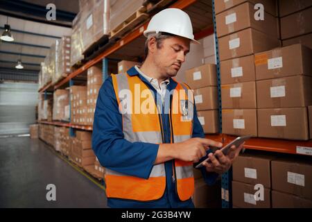 Portrait of a male warehouse supervisor in white hardhat using digital tablet in factory Stock Photo