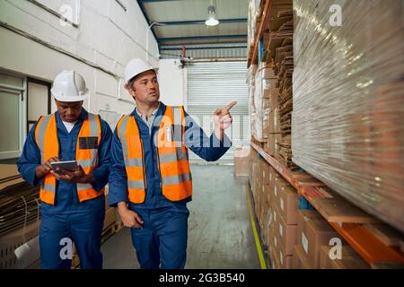 Two male worker checks stock and inventory with digital tablet computer in the retail warehouse full of shelves with goods Stock Photo