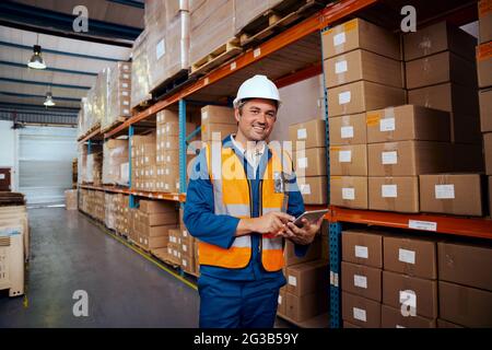 Smiling portrait of a male warehouse worker holding digital tablet in hand looking at camera Stock Photo