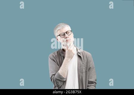 Pensive man with unusual appearance thinking about question, touching chin and looking away at copy space, contemplating about idea over blue studio b Stock Photo