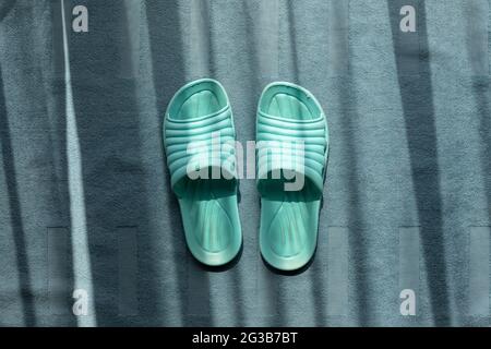Pair of green dirty indoor plastic sandals on fluffy blue carpet with shining sunlight from window. Stock Photo