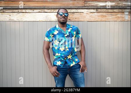 Young ?exican male wearing a stylish shirt and sunglasses standing outdoors leaning on the wall Stock Photo