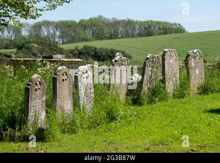 Old gravestones stand in a row in the graveyard at St Peter's Church in Rodmell near Lewes in East Sussex, UK Stock Photo