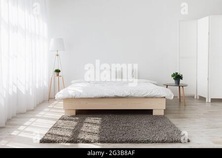 Real photo. Space at home with big comfortable double bed in elegant classic modern bedroom, interior design. Furniture on floor in light from window, Stock Photo