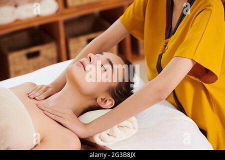 Close-up of therapist doing massage to young woman while she lying on bed with her eyes closed Stock Photo
