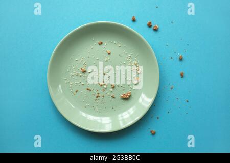 Emty white plate with some crumbs on light blue background. Finished party and holidays concept. Stock Photo