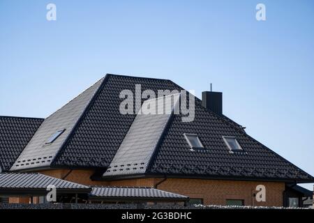 Brown corrugated metal profile roof installed on a modern house with a attic windows. The roof of corrugated sheet. Roofing of metal profile wavy Stock Photo